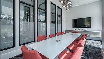 A conference room with a long white table and red chairs